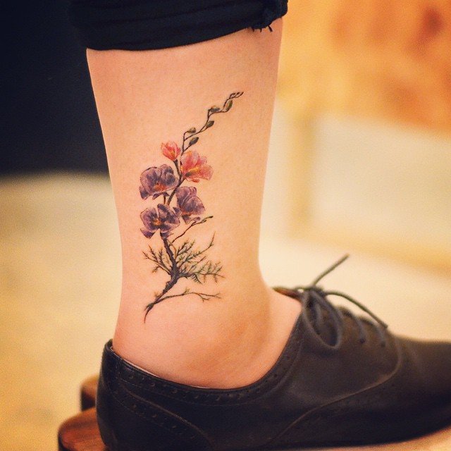 Tatuagem na perna feminina delicada: Flores e arte realista no tornozelo