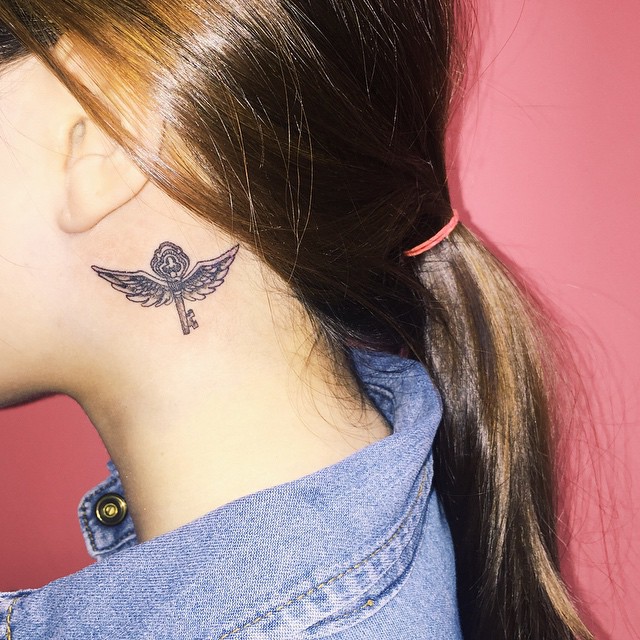 Linda tatuagem feminina atrás da orelha - Uma chave com asas.