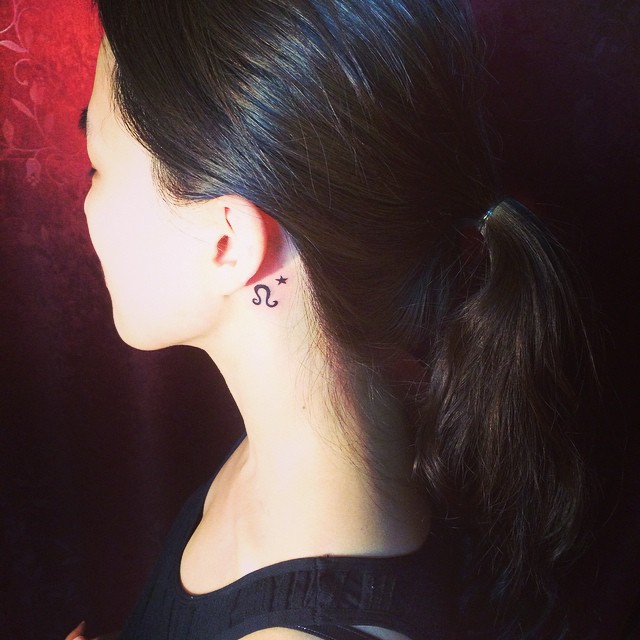 Tatuagem delicada atrás da orelha com motivo zodiacal.