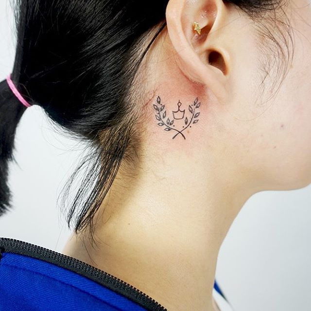 Tatuagem de ramos e coroa atrás da orelha.