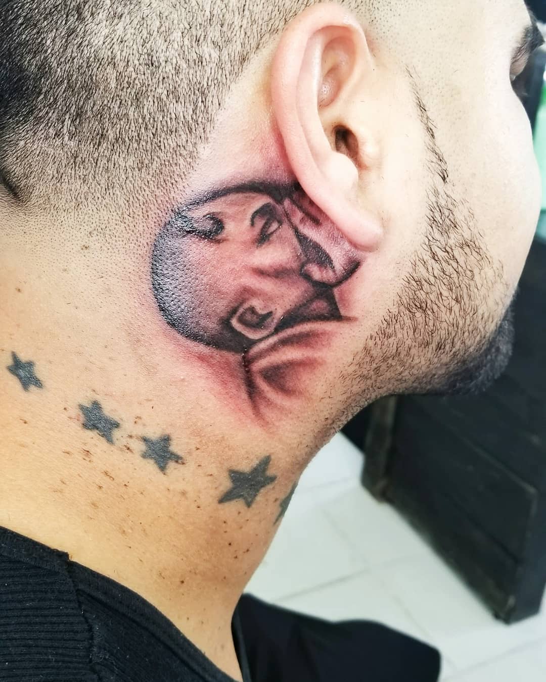 Tatuagem masculina atrás da orelha com motivo irreverente.