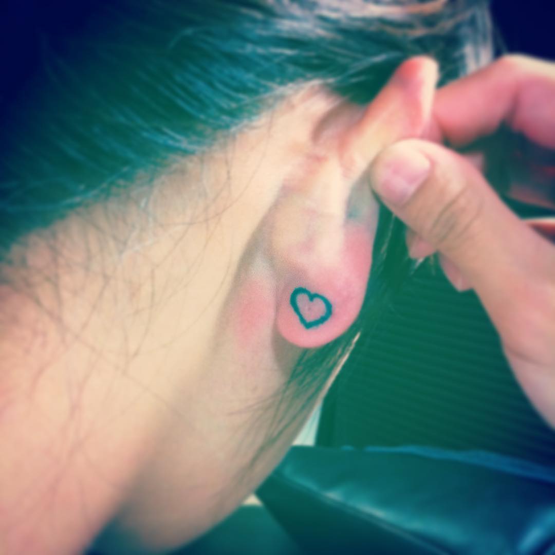 Coração pequeno tatuado atrás da orelha.