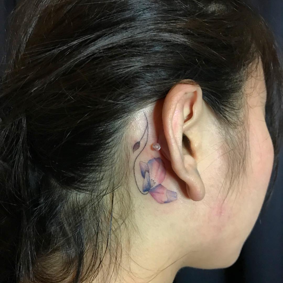 Tatuagem de flor aquarelada atrás da orelha, feminina e delicada.