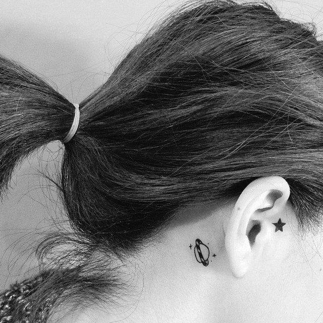 Tatuagem feminina atrás da orelha de um planeta.