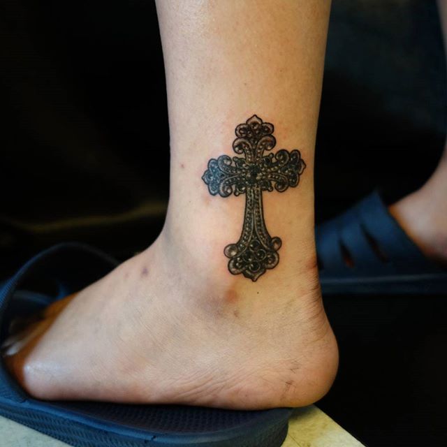 Tatuagem de cruz no tornozelo em estilo antiga ou medieval, com traços mais escuros