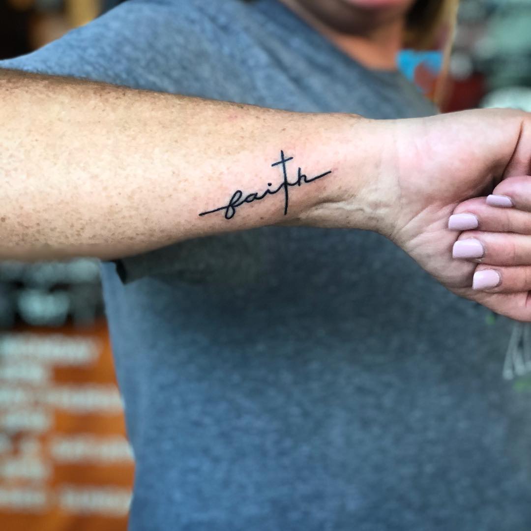 Tatuagem de frase: ‘’Fé’’ em inglês formando a cruz no braço