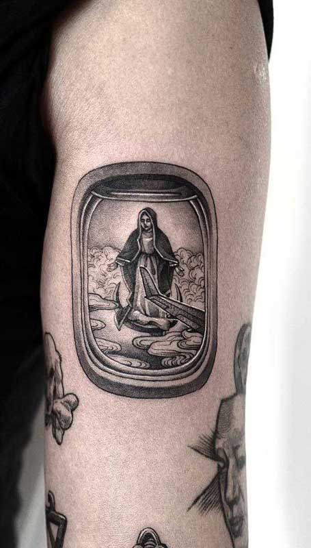 Aqui, a tatuagem de santa vem acompanhada de um cenário completo