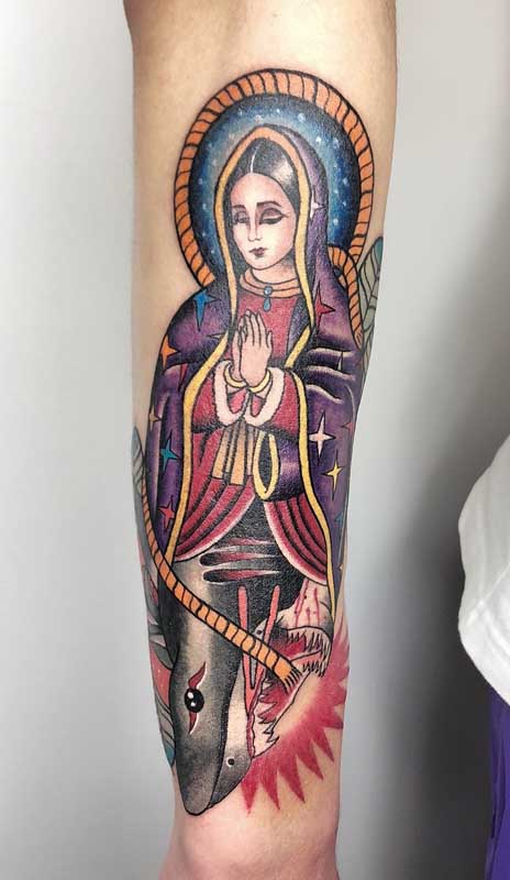 Tatuagem de santa no braço. Repare que a parte de cima traz a imagem da santa, enquanto a parte debaixo é um tubarão