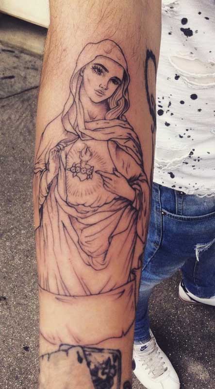 Tatuagem de Nossa Senha de Fátima no braço. O destaque aqui é o traço fino do desenho