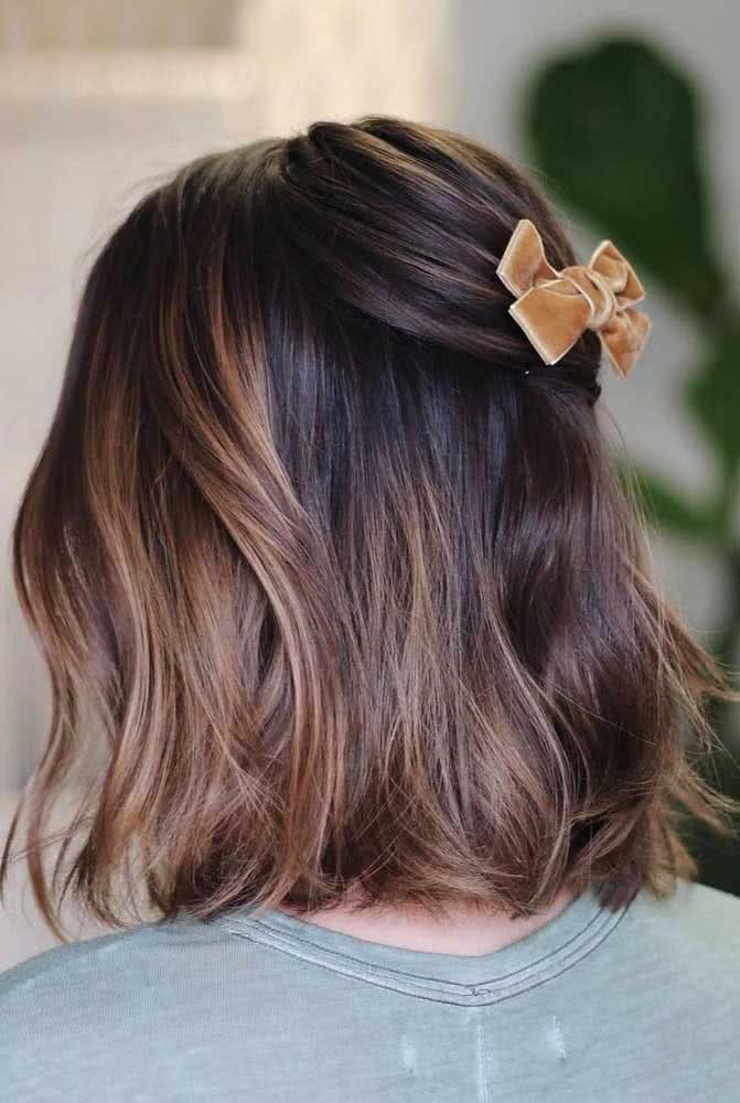 Com o cabelo dividido, junte somente as mechas de cima na parte de trás do cabelo com um lacinho para fazer outro penteado simples mas cheio de charme.