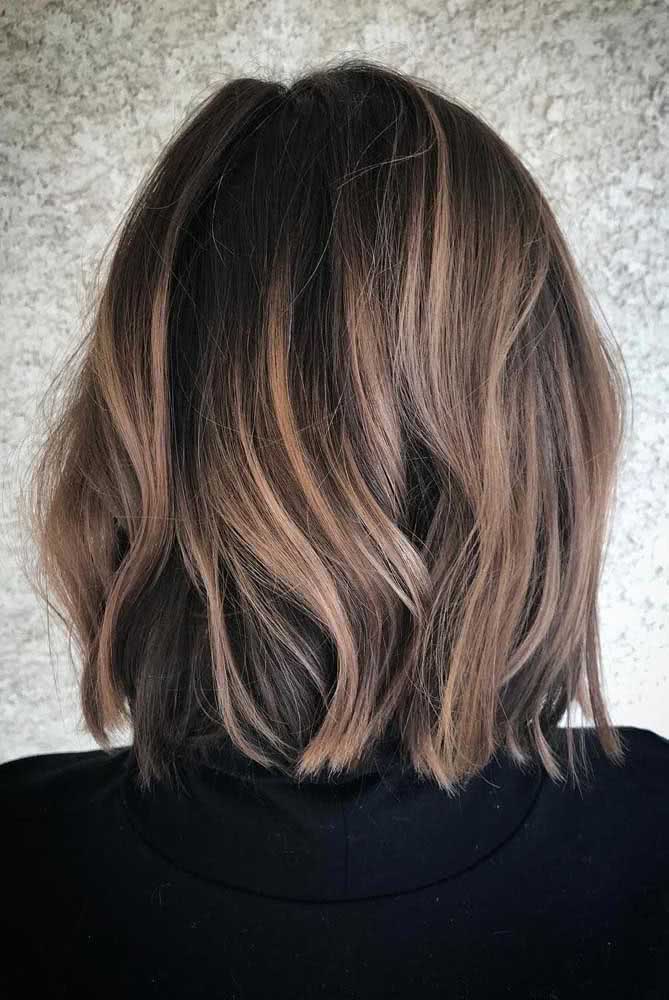 Uma iluminação contrastante e suave ao mesmo tempo nesse cabelo preto em long bob com mechas loiras na superfície. 