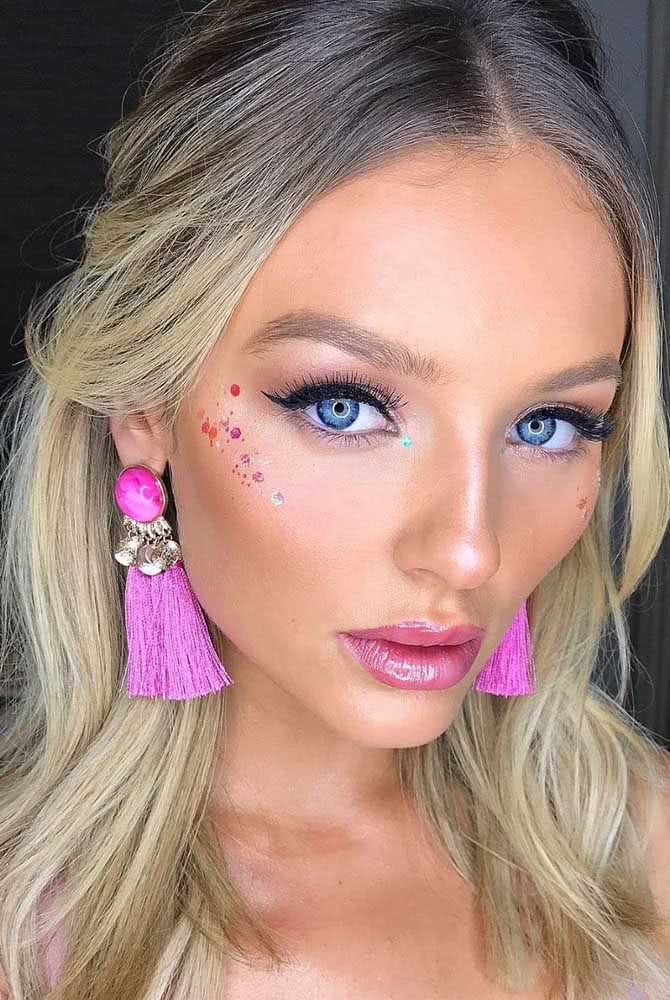 Já para festas, a maquiagem simples com batom gloss rosa, delineador e cílios alongados ganha um toque a mais com aplicação de uma linha de glitter e lantejoulas coloridas na lateral do rosto. 