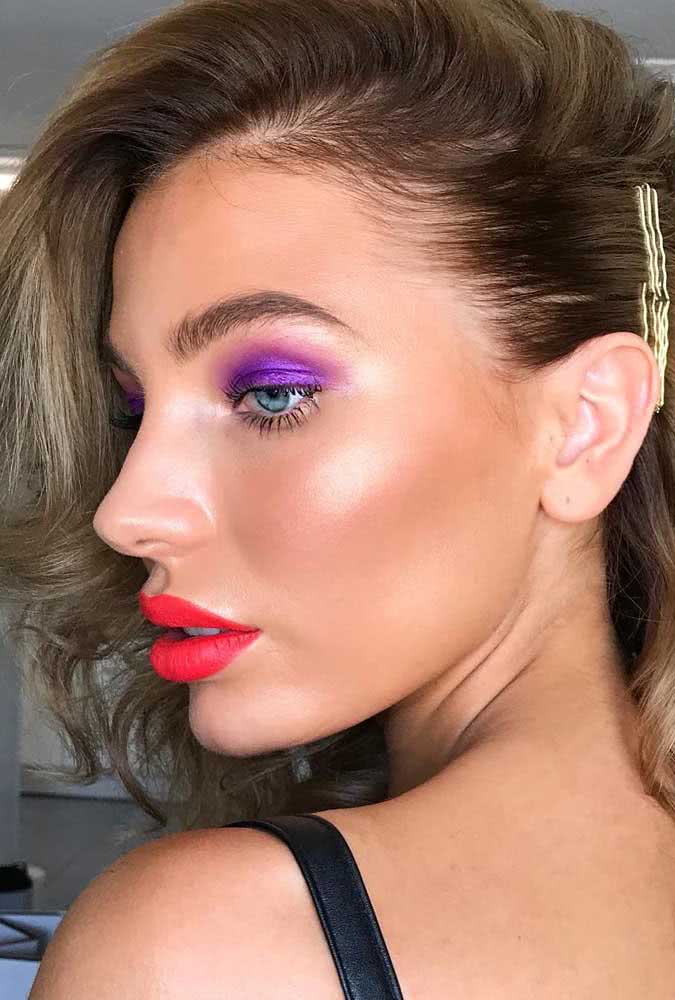 O vermelho do batom e o roxo da sombra ficam ainda mais vibrantes com a iluminação certeira desta maquiagem simples, mas cheia de personalidade. 