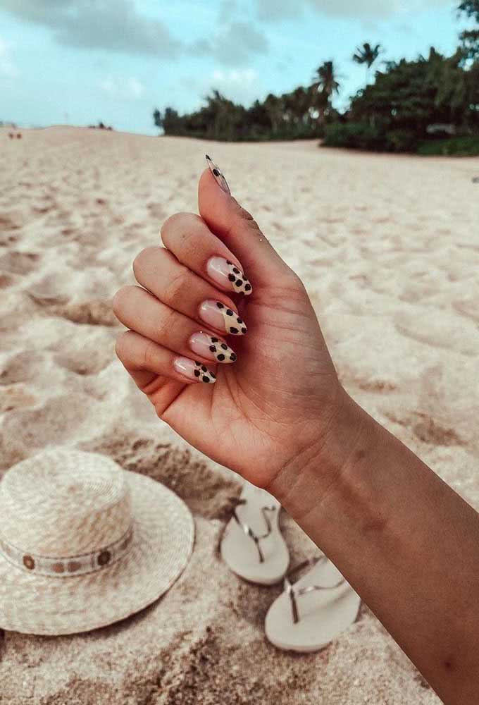 Seguindo a linha das laterais, uma half nail diagonal com parte seguindo o tom natural da unha e parte num amarelo pastel, com pintinhas pretas, criando um padrão de oncinha simplificado. 