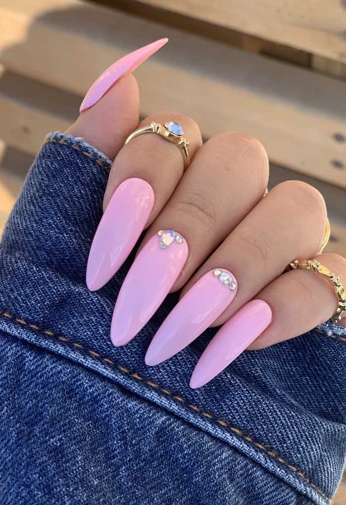 Unha stiletto longa com esmalte rosa clarinho com aplicação de pedra próximo à cutícula.