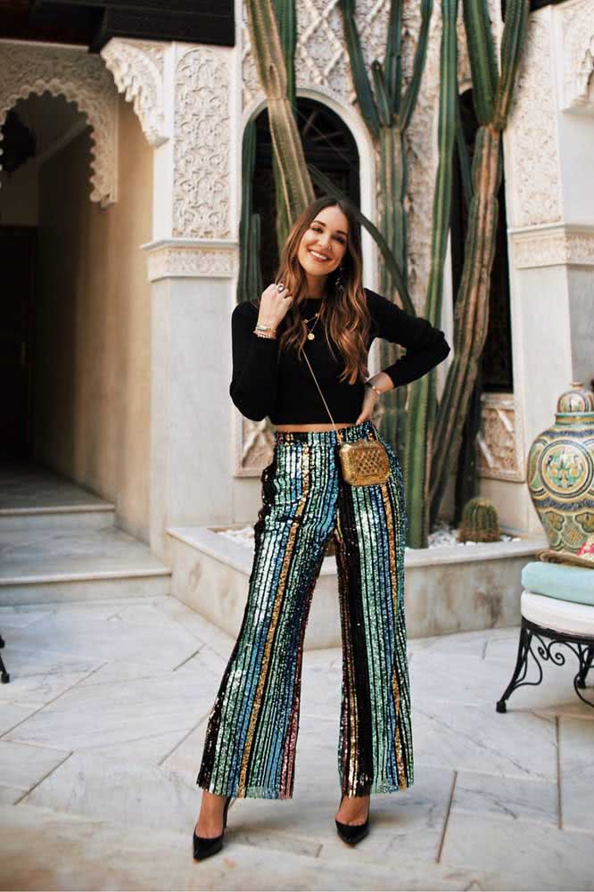 Calça pantalona listrada e brilhante com scarpin e blusa de manga longa pretos fazem um look glam perfeito para usar em passeios ou em festas.