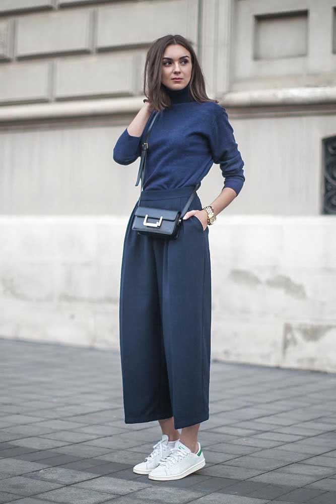 E num estilo streetwear, um look monocromático com calça pantalona e blusa com gola rolê azul e tênis branco.