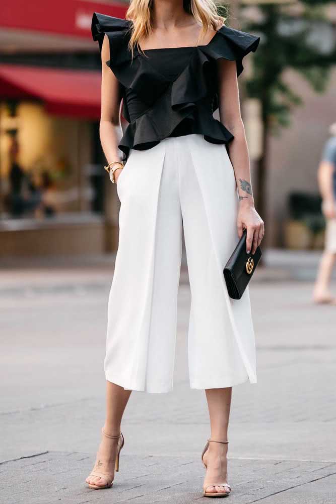 Calça pantalona social branca e blusa preta com manga curta babada formam um look sofisticado para o trabalho ou eventos sociais diurnos.