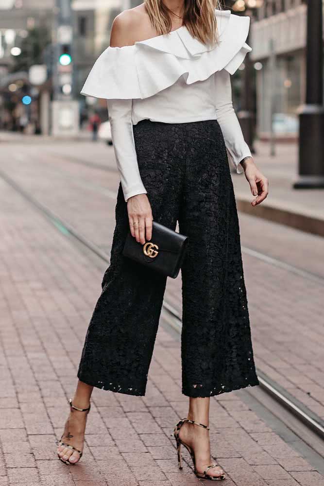 Textura e movimento neste look elegante com calça pantalona preta rendada e blusa de manga longa ombro a ombro branca com babados.