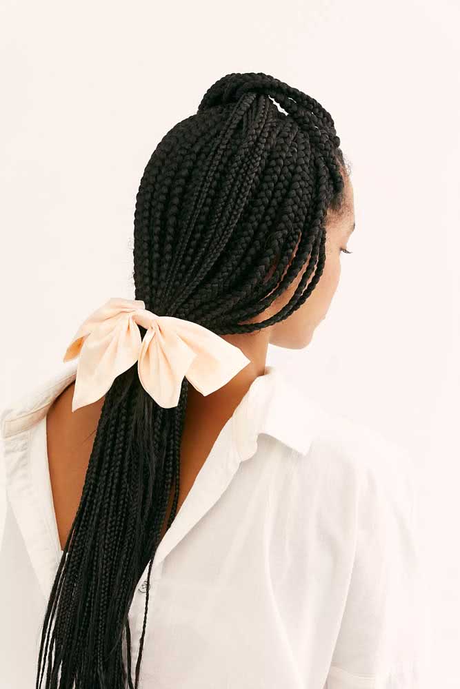 O cabelo todo trançado com box braids é extremamente versátil e permite uma série de outros penteados, como esse rabo de cavalo baixo super charmoso com laço de tecido. 