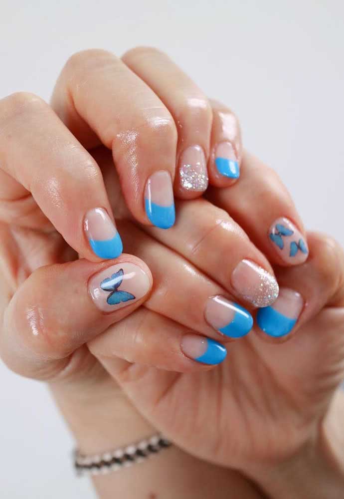 O adesivo de borboleta também traz um toque de delicadeza para esta composição com half nails azul anil e brilho.