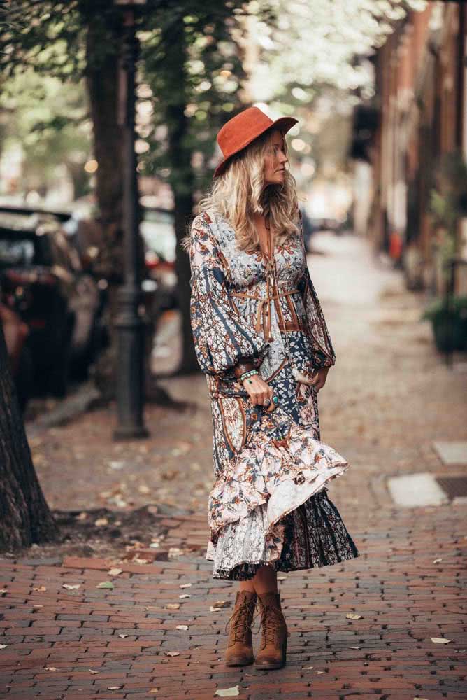 Num look que caracteriza perfeitamente o estilo boho, vestido estampado midi leve, chapéu e bota em uma combinação de azul claro com tons terrosos.