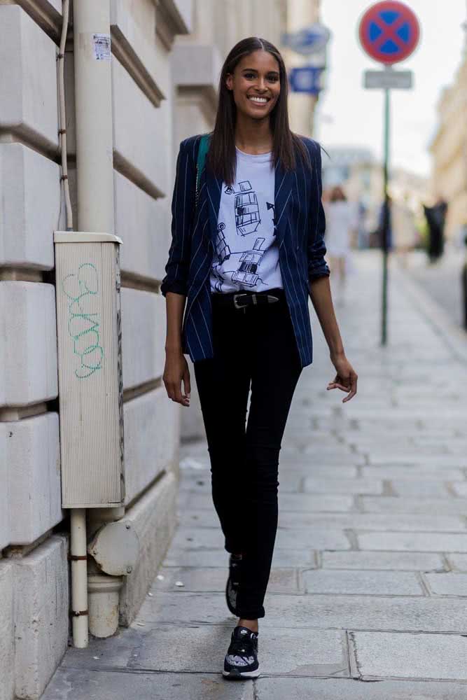 O blazer azul risca de giz finaliza este look moderno de trabalho com camiseta branca estampada, calça jeans e tênis.