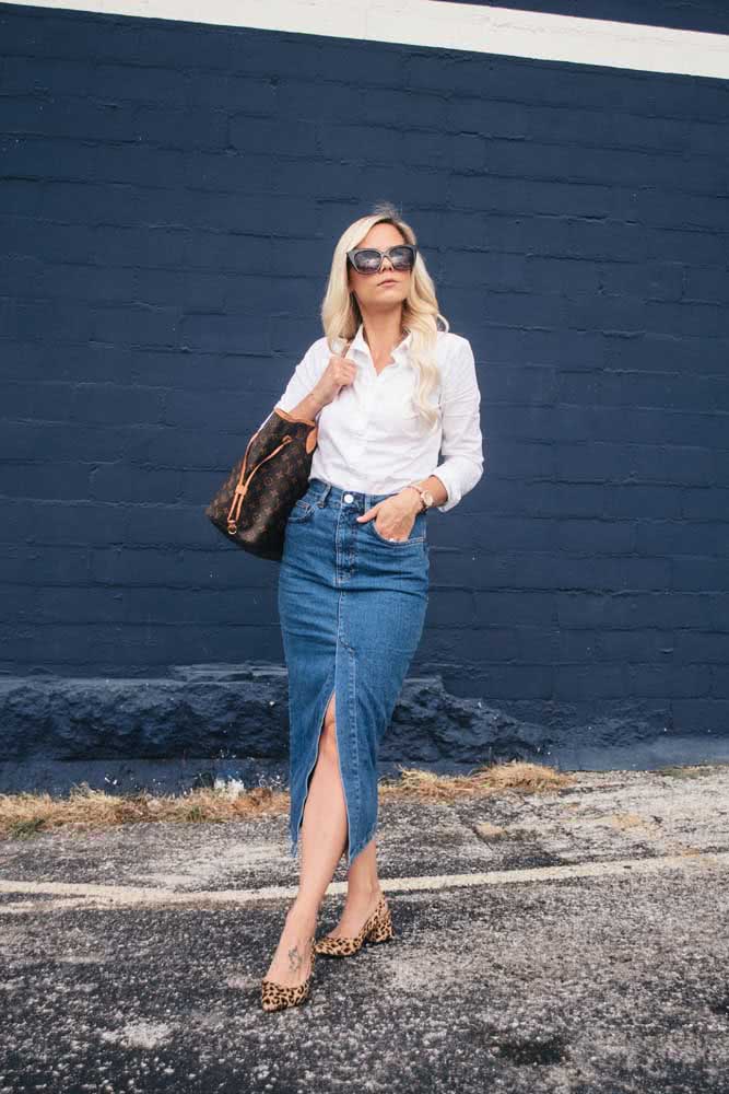 A saia midi é outra ótima opção para um look de trabalho. Neste exemplo, uma ideia cheia de personalidade com camisa branca, saia jeans com fenda e sapato com estampa de oncinha. 