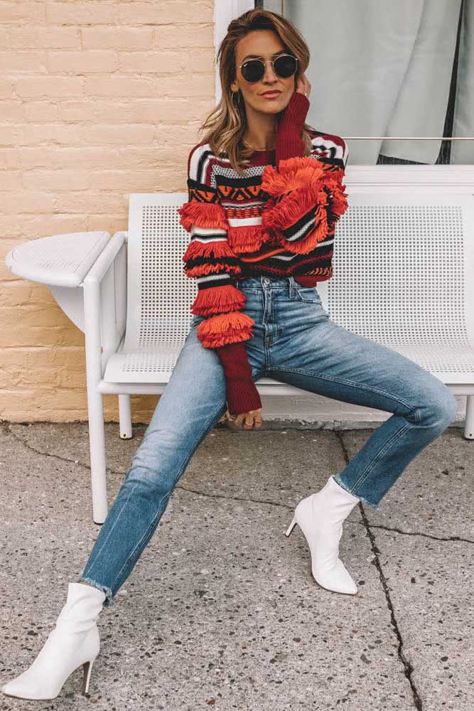 Um look nada básico com mom jeans, bota branca de salto e cano médio e um suéter cheio de padrões e movimento.