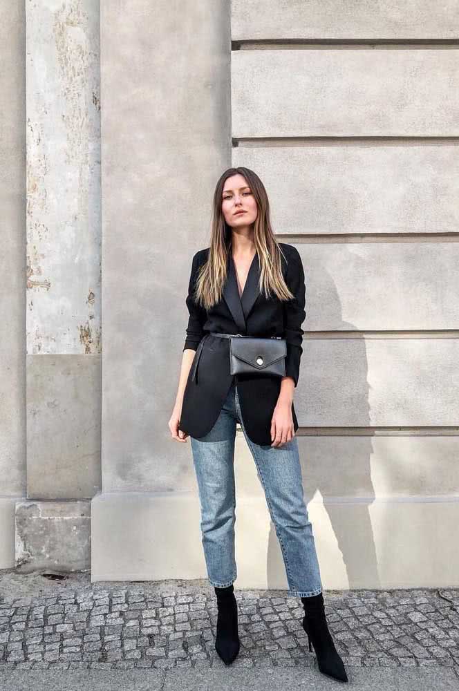 Já com bota de cano alto e bico fino, blazer preto acinturado com uma pochete, a mom jeans forma o visual perfeito de uma fashionista.