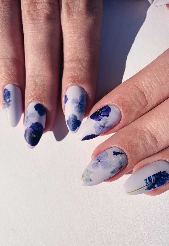 Unhas decoradas com flores azuis. O formato stilleto garante o toque de ousadia