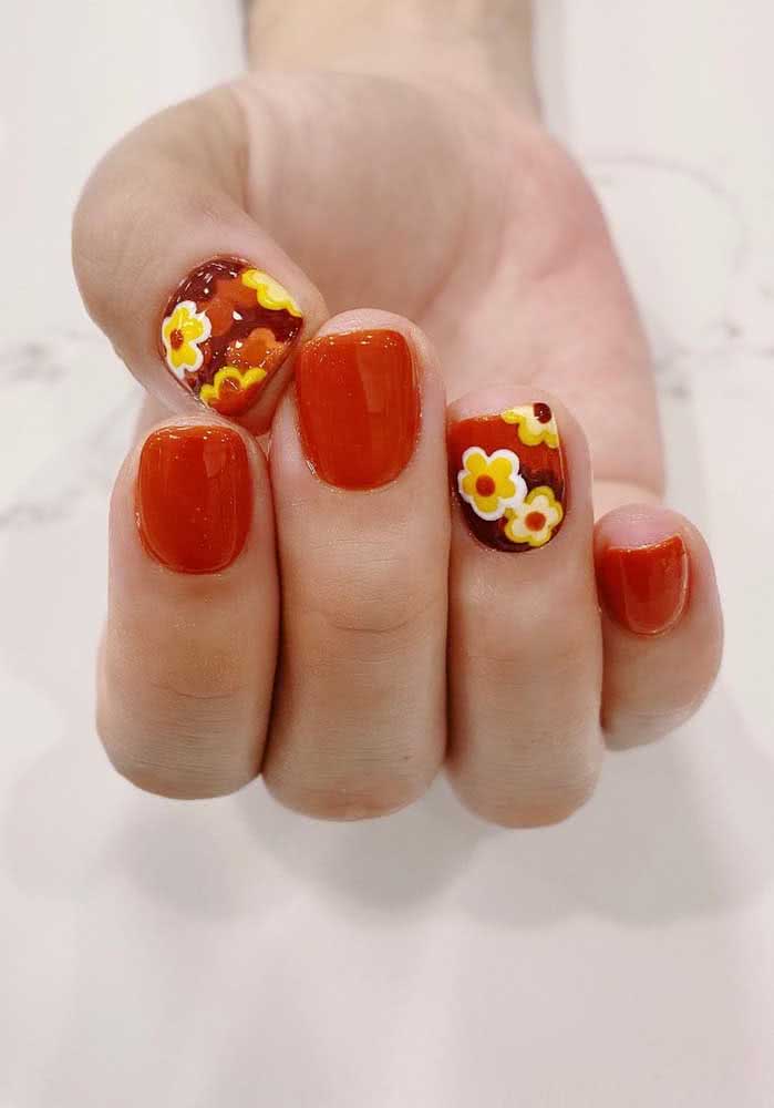 Unhas decoradas com flores amarelas sobre o esmalte vermelho