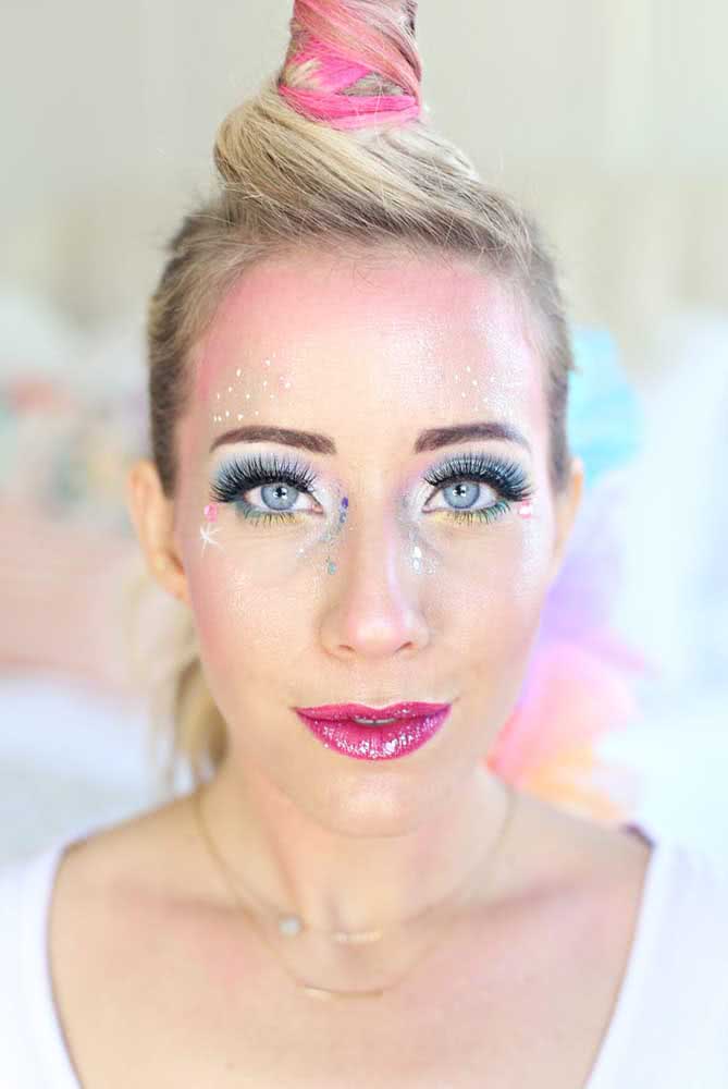 Maquiagem de unicórnio simples com sombra azul e pontos de luz por todo rosto. Repare que o chifre foi feito com o próprio cabelo da modelo
