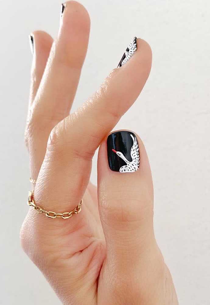 Além de padrões diferentes, as unhas também podem ser decoradas com desenhos, como o caso desse cisne no fundo preto