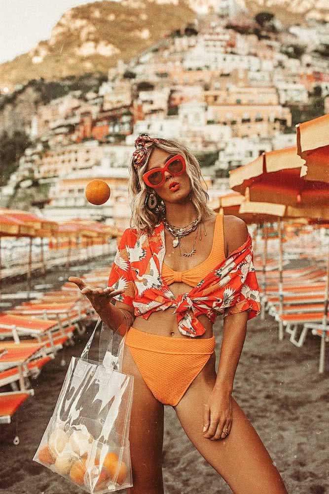 Look praia vibrante monocromático, com biquíni, óculos de sol e camisa amarrada na cintura em diferentes tons de laranja. 