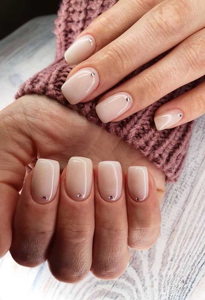 Unhas encapsuladas delicadas com um ponto brilhante se destacando no fundo nude.