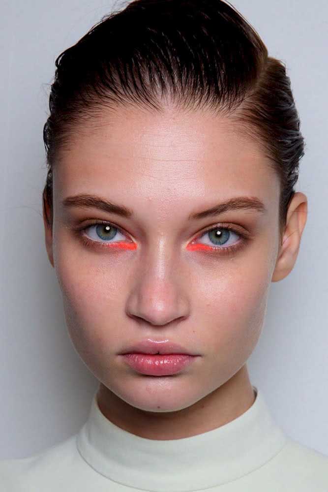 Maquiagem sutil ganha um toque a mais com um risco de lápis laranja neon no canto interno do olho.