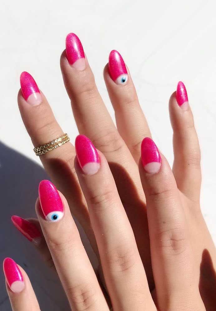 Uma tendência na nail art é a inserção de outros tons ou até mesmo desenhos na área arredondada próxima à cutícula, como estes olhinhos vigilantes nas filhas únicas dessas unhas decoradas rosa pink.