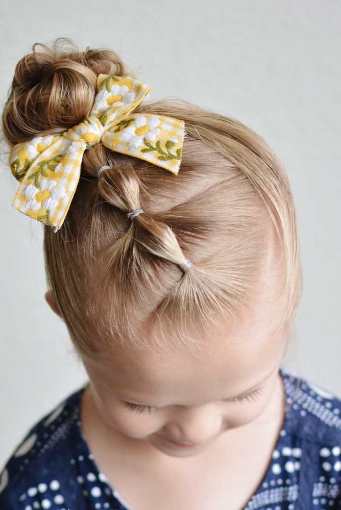 O uso de elásticos cria um efeito de trança embutida no topo da cabeça, um detalhe a mais neste penteado para criança com coque. 