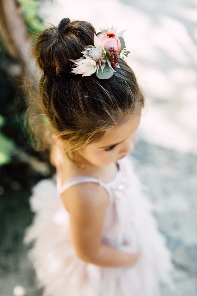 Outra ideia de penteado infantil para festas é um coque alto com um arranjo de flores. 