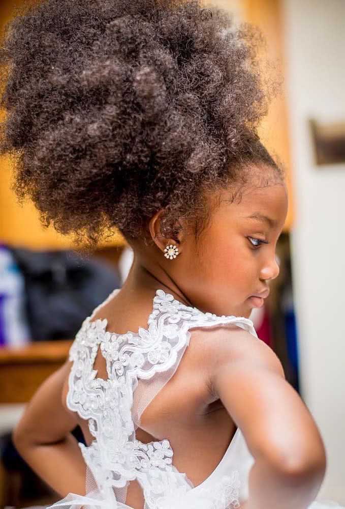 Um penteado que valoriza o volume e a textura do cabelo crespo, em um afro puff alto.