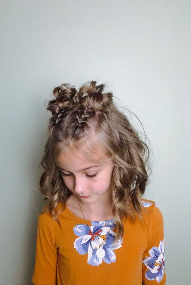 Um penteado simples e divertido para criança com cabelo ondulado, com duas tranças paralelas no topo da cabeça que se transformam em coques bagunçadinhos.