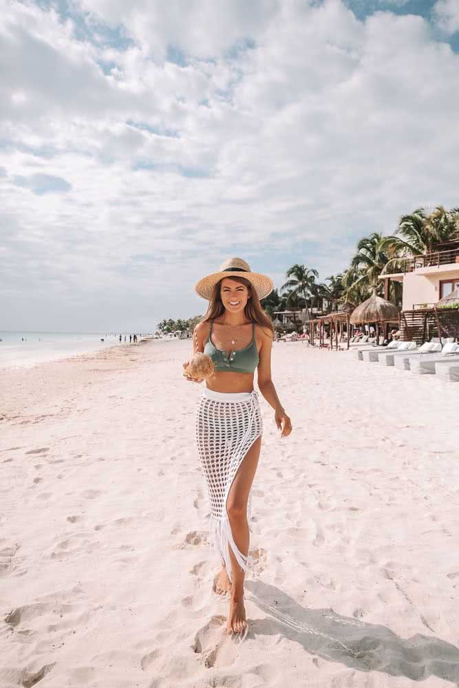 A saia midi de macramê com fenda e franjas traz mais movimento para este look praia com biquíni verde e chapéu de palha.