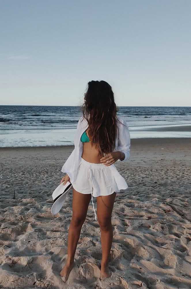 Shorts e camisa aberta de linho branco com o top do biquíni aparecendo num visual leve e descontraído para curtir o dia e a noite na praia.