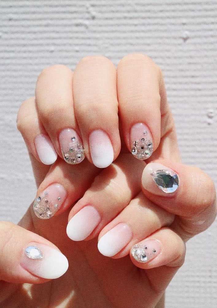 A aplicação de strass de diferentes tamanhos em conjunto com o glitter traz ainda mais brilho para essas unhas decoradas com degradê branco.