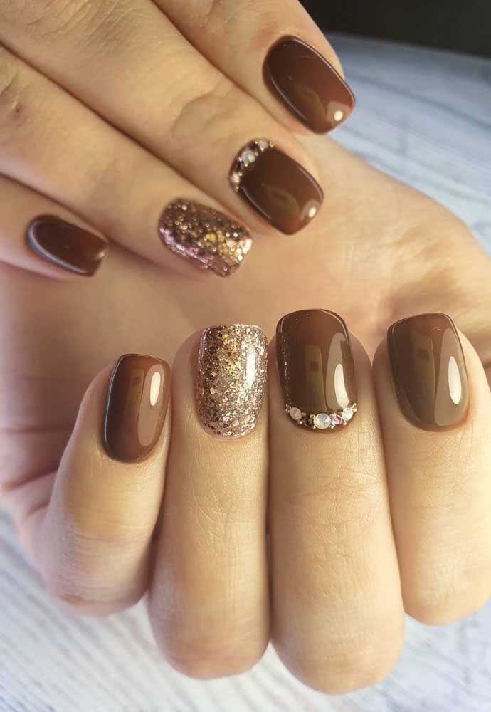 Unhas decoradas com pedras e glitter em marrom e dourado.