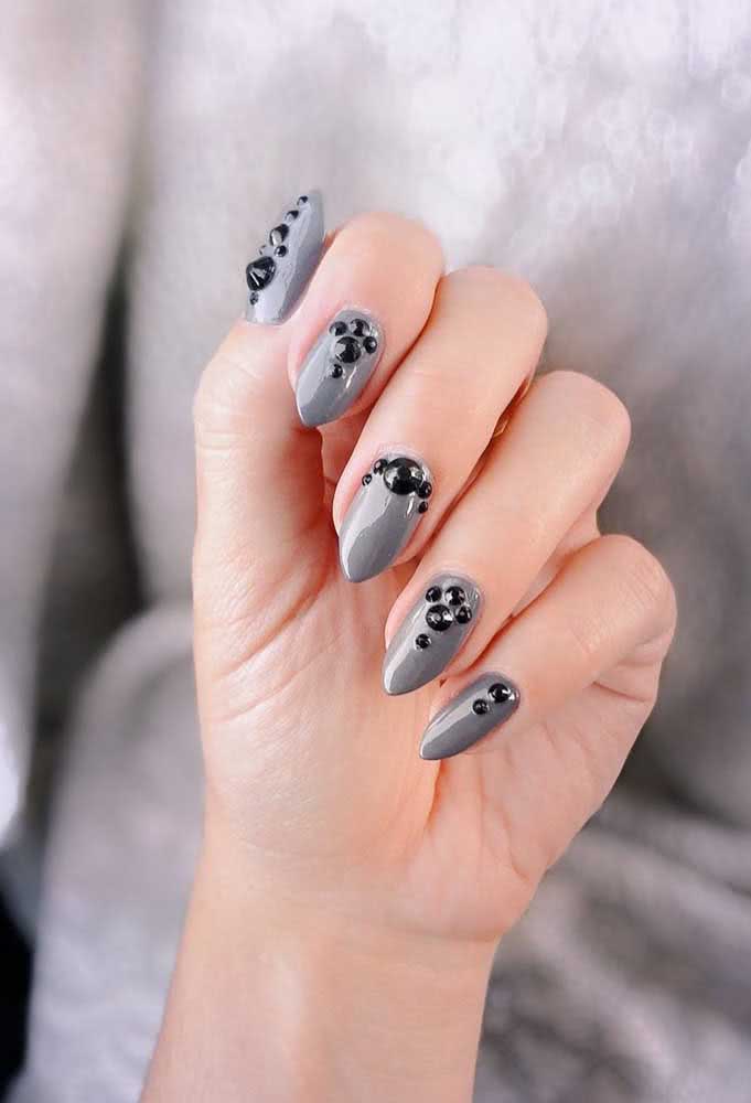 Unhas decoradas com pedras pretas em tamanhos diferentes.