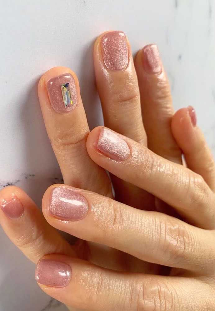 Unhas decoradas com aplicação de uma pedra retangular na filha única sobre o fundo rosa claro com glitter.