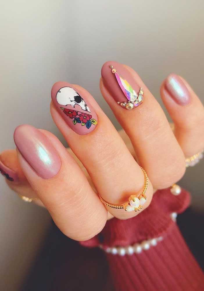 Para um visual cheio de estilo e atitude, unhas decoradas com pedra furta-cor e adesivo de flores e caveira sobre o esmalte rosa.