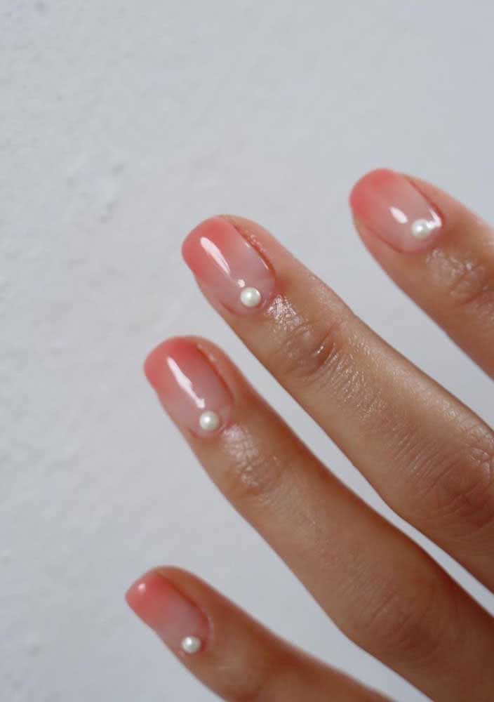 E que tal usar pérolas nas suas unhas decoradas com pedras? Neste exemplo, elas trazem delicadeza e elegância para a pintura em degradê rosa claro. 